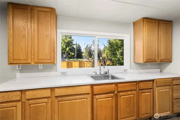 Bright kitchen workspace showcases ample cabinetry & counters, new SS sink and a new double-paned vinyl window bringing in natural light.