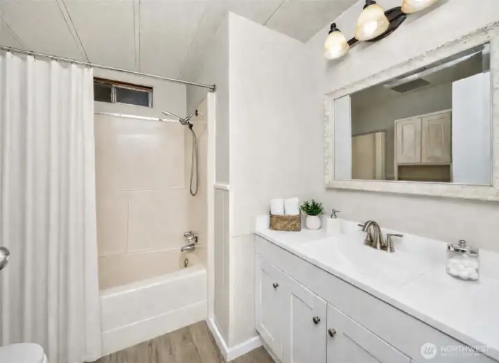 Full bathroom offers a shower/tub combo, new vanity, new LVP flooring, and modern lighting updates.  (accessories in photo virtually staged)