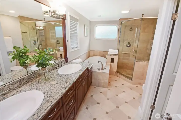 This sophisticated bathroom features modern amenitites, dual vanities all in warm natural stone of travertine. The shower features two shower heads. The door to the walk-in-closet can be seen on the right.