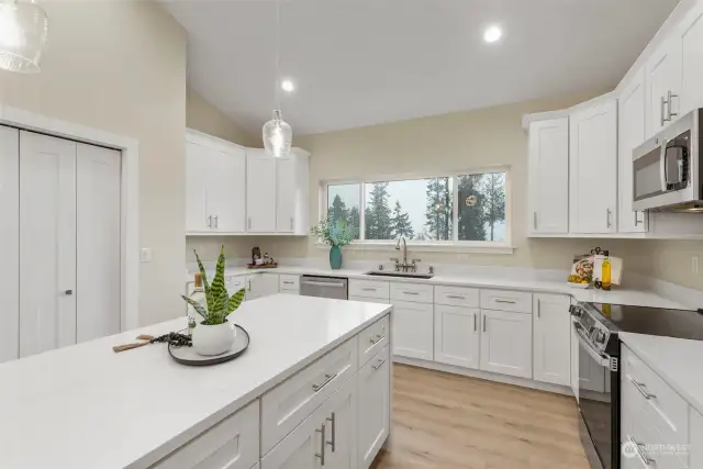 Kitchen is open and bright, with stainless appliances, solid quartz counters, and white shaker cabinetry.