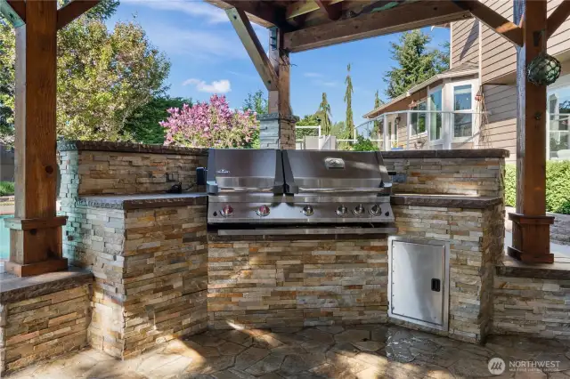 Stone patio with fireplace, built-in Napoleon grill, and fir-beamed steel roof—designed for year-round gatherings.