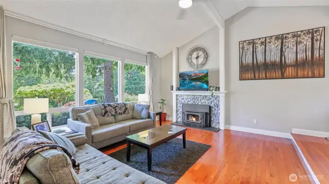 This stunning living room features a gas fireplace, vaulted ceilings, and wall-to-wall windows that flood the space with natural light