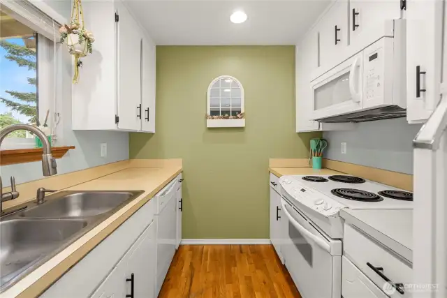 This view showcases the kitchen's layout, featuring a white electric range with a matching microwave above. The fresh green accent wall adds warmth and frames the decorative pass-through shelf at the end of the space.