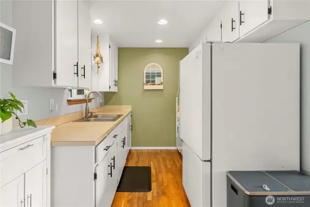 An extended view down the galley kitchen emphasizes the continuous cabinetry and countertop workspace. Overhead recessed lighting and a thoughtful layout create a clean, organized flow for daily meal prep and storage.