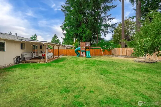 Perfect for play and gatherings, this fully fenced yard includes a two-slide playhouse, climbing wall, and room for lawn games. The lush grass and wood fencing create a private, inviting environment.