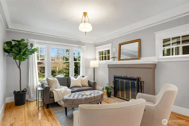 The living room features high ceilings,  original wood windows, the original tile  fireplace, and detailed millwork.