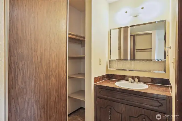 Second Closet with shelves in the Primary Bath Area- see a reflection of the First closet in the mirror. Commode/Shower area to the right.