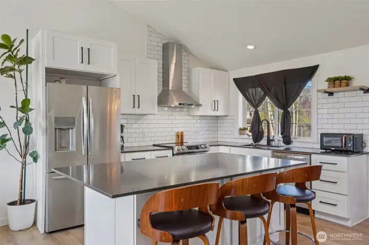 Updated kitchen features quartz countertops, custom cabinetry, stainless steel appliances, tile backsplash, and an oversized island.