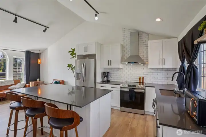 Updated kitchen features quartz countertops, custom cabinetry, stainless steel appliances, tile backsplash, and an oversized island.