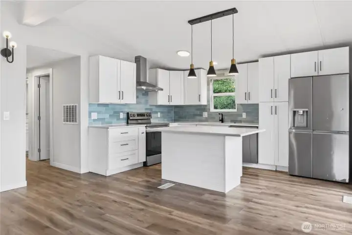 Kitchen with Blue Tile Backsplash, Stainless Range, Quartz Island, and Hallway to Bedrooms