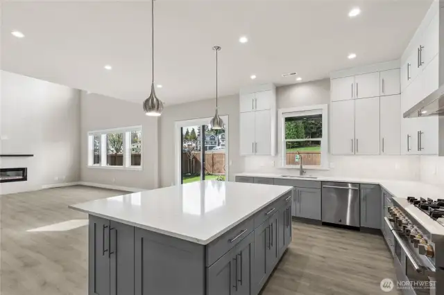 Bright and modern gourmet kitchen featuring a large quartz island, two-tone cabinetry, stainless steel appliances, and designer lighting. Open-concept layout flows seamlessly into the dining and living areas—perfect for entertaining.