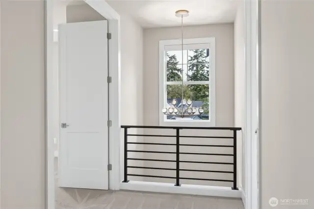 Upper landing with modern horizontal railing and large window showcasing natural light and treetop views. A stylish chandelier adds a contemporary touch to this bright transitional space.