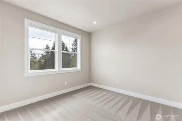 Secondary bedroom with soft neutral tones, large windows framing treetop views, and plush wall-to-wall carpeting. A bright and peaceful space ideal for guests, a home office, or a nursery.