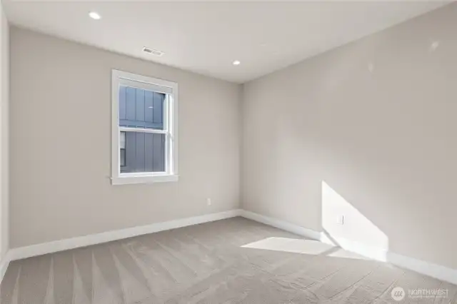 Cozy bedroom with soft neutral tones, plush carpeting, and recessed lighting. A large window provides natural light and a peaceful setting—perfect for a guest room, office, or additional sleeping space.
