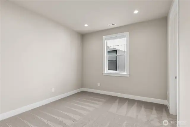 Cozy bedroom with soft neutral tones, plush carpeting, and recessed lighting. A large window provides natural light and a peaceful setting—perfect for a guest room, office, or additional sleeping space.