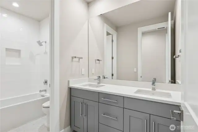 Modern full bathroom featuring a dual-sink vanity with quartz countertops, sleek cabinetry, and a tiled shower-tub combo with built-in niche. A bright and functional space with clean, contemporary finishes.