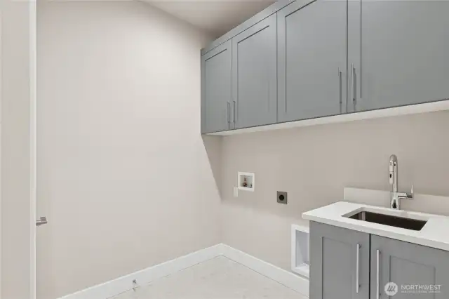 Well-appointed laundry room featuring upper and lower cabinetry for storage, a deep utility sink with modern faucet, and dedicated hookups for washer and dryer. A bright, efficient space designed for everyday convenience.