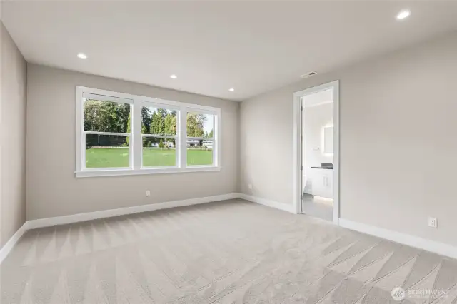 Spacious primary bedroom featuring plush carpet, recessed lighting, and a wall of windows that fill the room with natural light and peaceful backyard views. Includes direct access to a private en-suite bath.