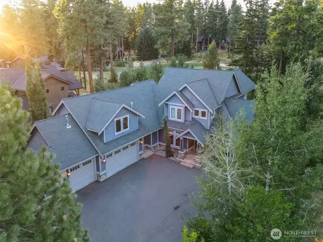 A striking aerial view of this mountain-lodge estate showcasing its welcoming front entry, generous driveway, and rare 3-car garage. Surrounded by evergreens and privacy landscaping, this home sits in the heart of Suncadia’s premier golf community.