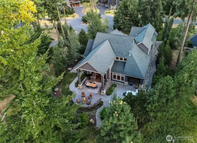 Nestled among pines, this view captures the home’s expansive covered patio, firepit lounge, hot tub retreat, and built-in outdoor kitchen — all set against a backdrop of winding paths and private forest-edge serenity.