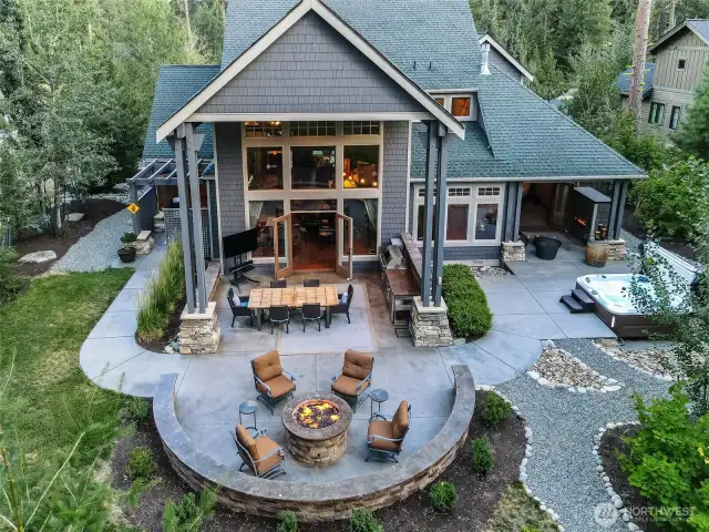 This close-up drone view reveals the thoughtfully designed outdoor experience: a covered outdoor kitchen and dining space, curved firepit lounge with built-in seating, and spa area just off the primary suite — every inch crafted for luxury and connection.