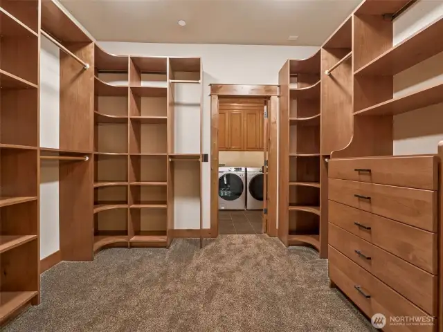 Expansive walk-in closet features a full built-in organization system with open shelving, dual hanging bars, soft-close drawers, and elegant corner display units. Direct access to the laundry room adds seamless everyday convenience.