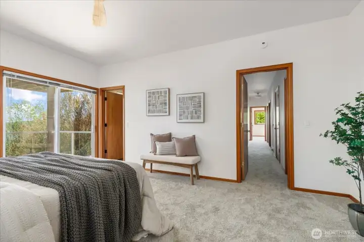 Primary bedroom with slider to the view deck and door to the ensuite bath at left and looking down the hall toward the other 3 bedrooms, full bath, and laundry/mechanical room.