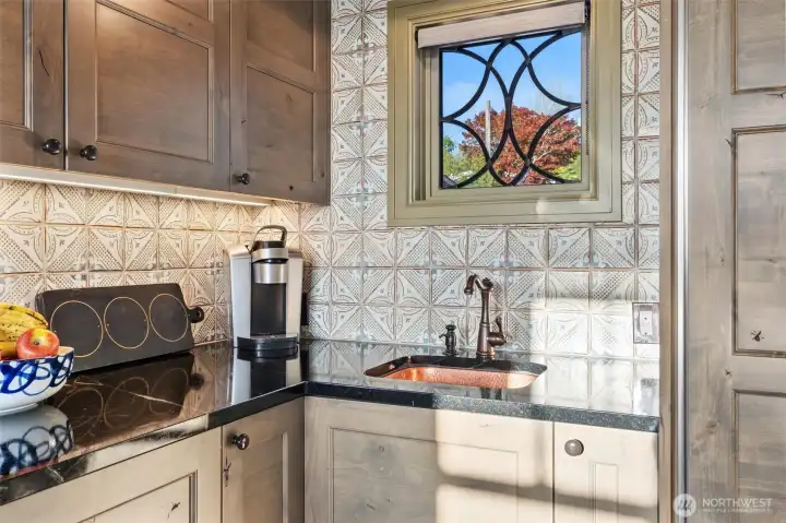Throughout the home, you’ll notice thoughtfully crafted cased openings and distinctive leaded glass windows that add character and charm. In the kitchen, one such window sits above a beautifully hammered copper sink, creating a convenient secondary prep area that’s as functional as it is visually striking.