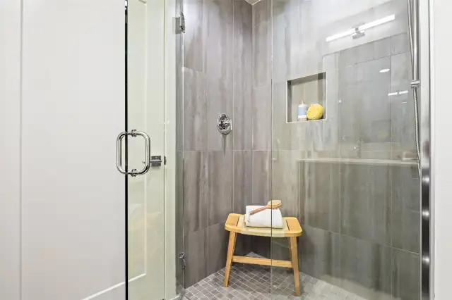 This luxe walk-in shower features oversized tiles and glass doors, a built-in niche, and calming design touches.