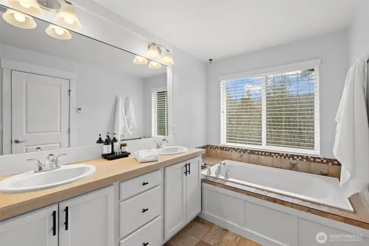 Double vanity with soaking tub looking out to greenspace.