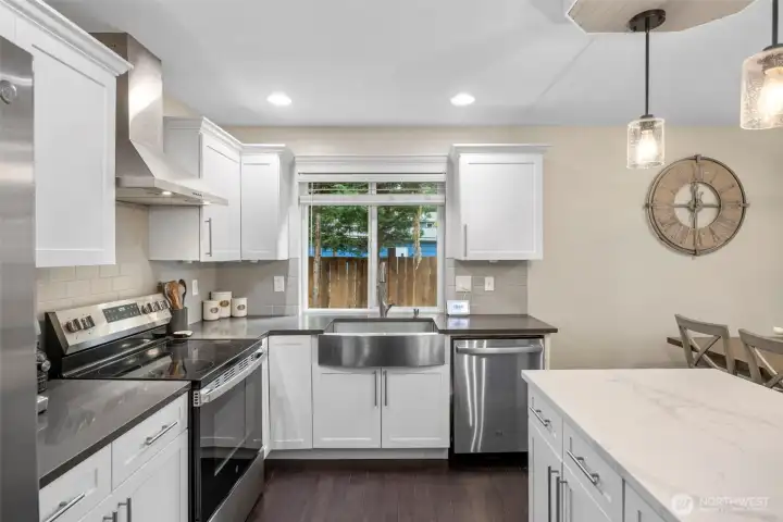 Spacious kitchen with a large farmhouse sink, expansive island, quartz countertops, tile backsplash, gorgeous cabinetry, & stainless steel appliances. Kitchen is open to dining and living room.