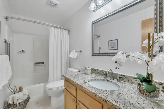 The elegant, updated guest bath showcases sleek slab granite countertops, stylish tile flooring, and a modern LED exhaust fan and light.