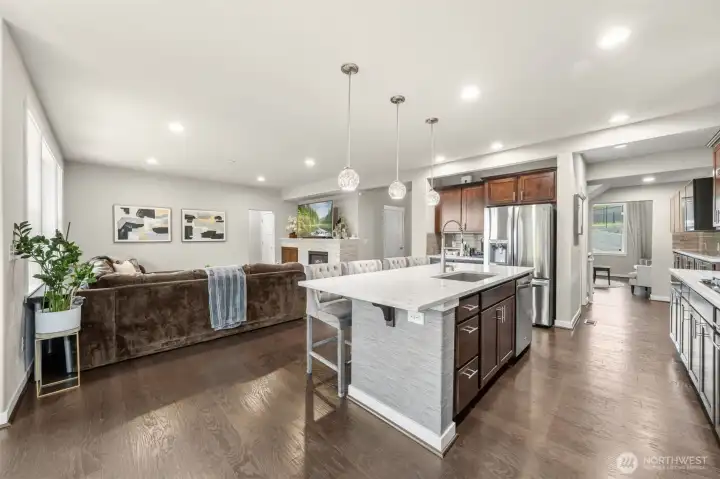 A quartz-topped island with bar seating, a stone fireplace, and clean sightlines to every main living space — this is where the home truly comes together for everyday living and effortless entertaining