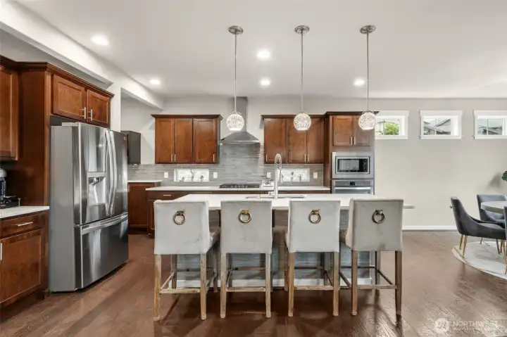Rich cabinetry, full stainless steel appliance suite, tile backsplash, pro-style range hood, and a large center island with seating for four — a kitchen that performs as beautifully as it looks.