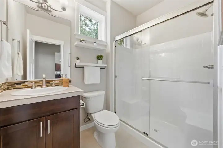 Conveniently serving the main level, this 3/4 bath features a mosaic tile backsplash, rich wood cabinetry, and a full glass-door shower — clean, functional, and thoughtfully finished.