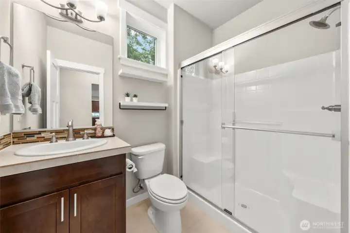 Conveniently serving the main level, this 3/4 bath features a mosaic tile backsplash, rich wood cabinetry, and a full glass-door shower — clean, functional, and thoughtfully finished.