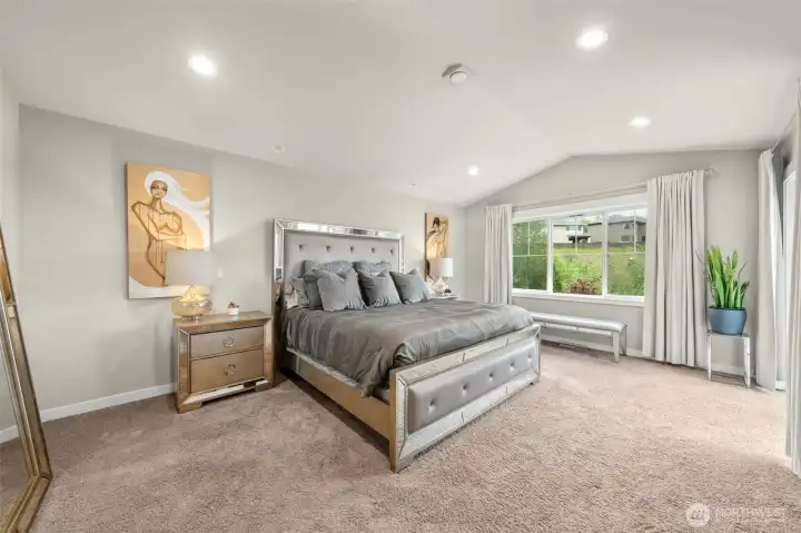 The primary suite is a true retreat — generously sized with vaulted ceilings, plush carpet, and a large window that fills the room with natural light and green views.