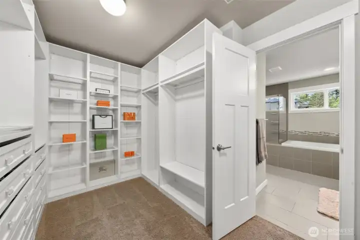 A second walk-in closet offers custom white built-ins with dedicated shelving, hanging space, and drawer storage — with direct sight lines into the en-suite bath, making this primary suite truly function like two separate dressing spaces in one.