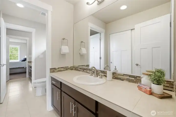Shared between bedrooms 3 and 4, this Jack and Jill bath features a wide vanity with mosaic tile backsplash, rich wood cabinetry, and a private water closet — thoughtfully laid out for two rooms to share without compromise.