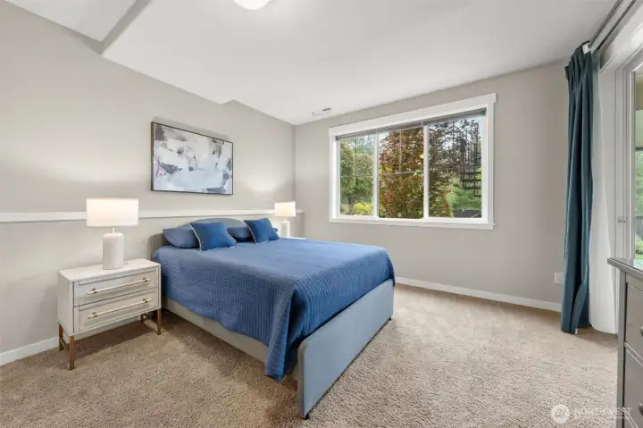 Bedroom 5 on the lower level offers a private retreat with a large picture window framing mature seasonal foliage, plush carpet, and direct access to the backyard — ideal for guests or extended family.