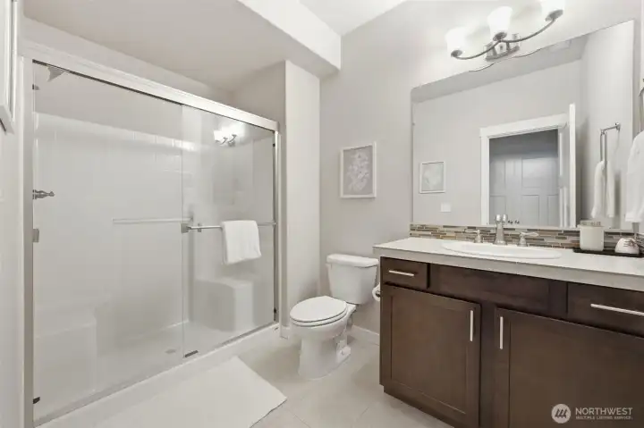 Serving the lower level, this 3/4 bath features a glass-door walk-in shower, wood cabinetry, mosaic tile backsplash, and tile flooring — a fully self-contained bath that makes the lower level function independently from the rest of the home.