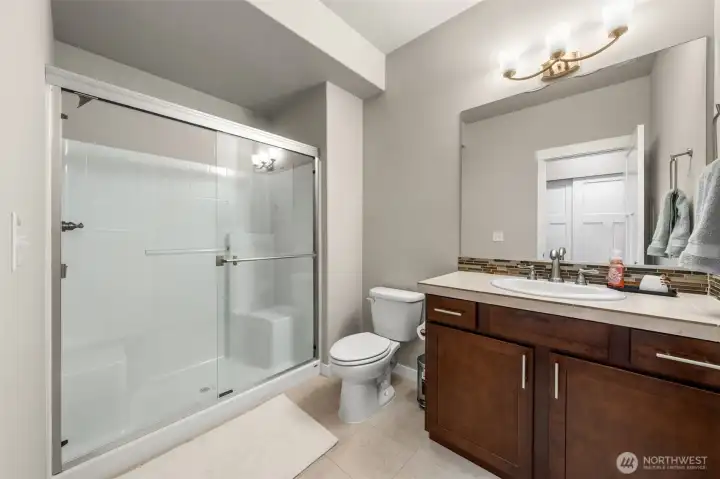Serving the lower level, this 3/4 bath features a glass-door walk-in shower, wood cabinetry, mosaic tile backsplash, and tile flooring — a fully self-contained bath that makes the lower level function independently from the rest of the home.