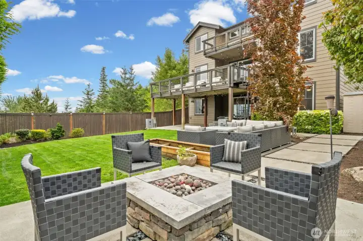 Gather around the stone fire pit and take in everything this backyard has to offer — a generous lawn, multiple seating zones, covered lower patio with string lighting, and an upper deck above.