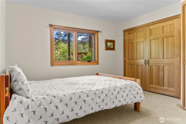 Guest bedroom with bright window views of forested surroundings.