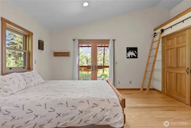 Spacious upstairs primary suite with vaulted ceilings, balcony access, large closet, and custom ladder to loft storage.