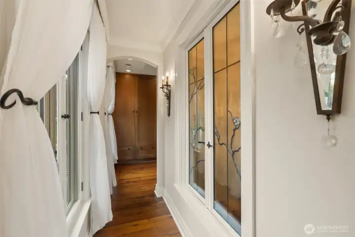The hallway showcases elegant Mesolini glass windows, offering a vantage point over the staircase and a light filled entry towards the primary closet.