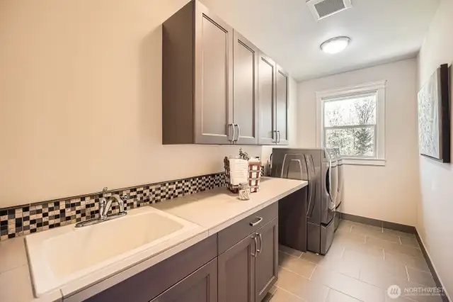 Spacious laundry room with utility sink, ample storage cabinets, designated dirty laundry area, and oversized front-load washer and dryer—offering a functional and efficient space for home upkeep.