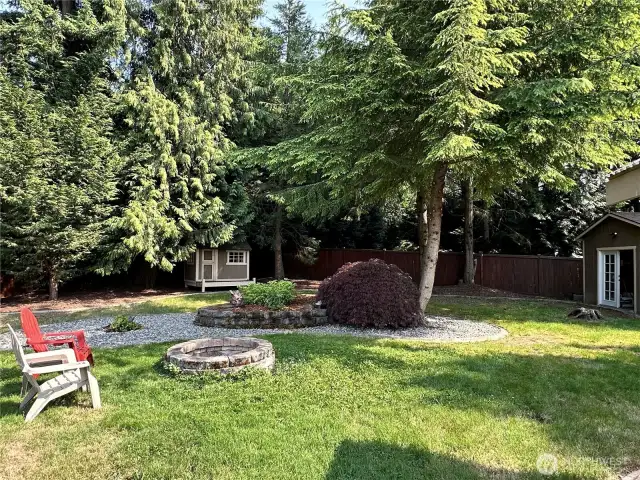 View of the fire pit area with playhouse/storage/art studio as well as the shop in back round. So much space on this lot makes it feel like a mini estate.