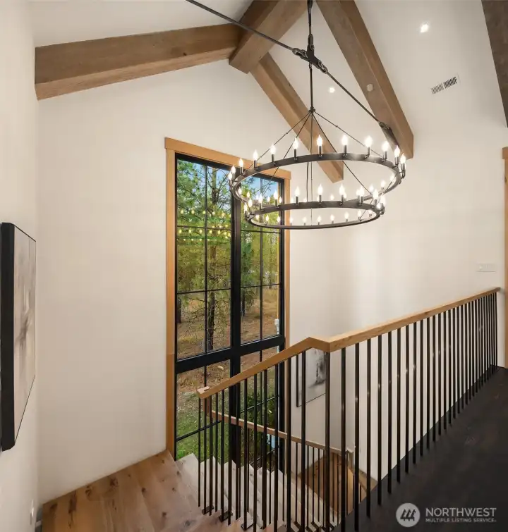 Entryway lights are built into the ceiling beam steel tie-rods, for a unique blend of  structure and elegance. Beams are white oak, with wire brush texture and custom  stain. The bridge is made from solid Doug Fir beams glued and thru bolted together to  create a one piece monolithic plank between the two wings of the upper level.