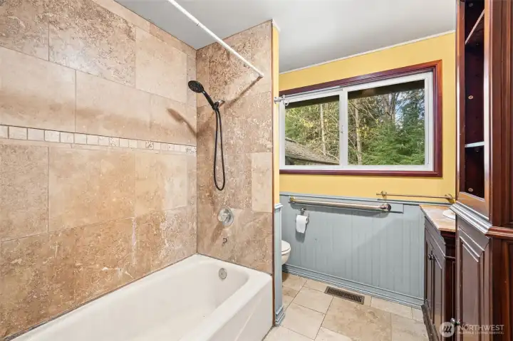 Full main hall bath with tiled shower surround, window for natural light, and functional layout. Ready for updates to create a fresh, modern space.